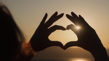 Yakın, kadın elleri arka planda gün batımı ile kalp şekli yapar, yavaş hareket