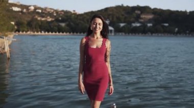 Kadın iskelede yürür, gülümsüyor, arka planda dağlar ve göl, yavaş hareket