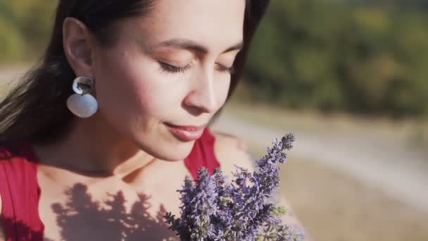 女性の肖像画は、野生の花の花束を保持し、それらを嗅ぎ、スローモーション — ストック動画