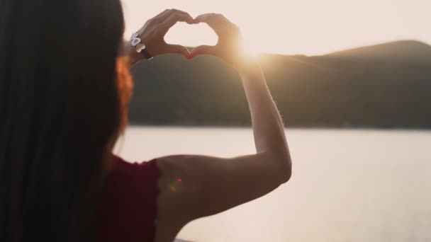 De cerca, las manos de la mujer hace que la forma del corazón con puesta de sol en el fondo, cámara lenta — Vídeo de stock