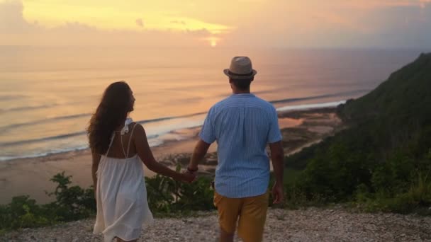 Casal de amantes de mãos dadas ir ao penhasco olhar para o pôr do sol bonito, câmera lenta — Vídeo de Stock