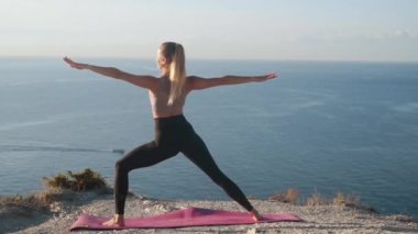 Genç kadın dağın tepesinde esneme yapıyor, arka planda deniz, yavaş çekim