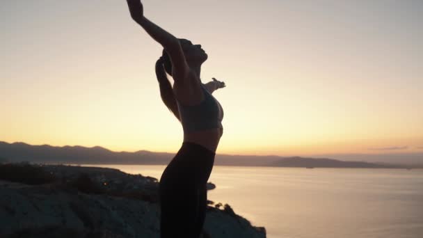 Mulher bonita pratica ioga, medita ao nascer do sol com vista para o mar, câmera lenta — Vídeo de Stock