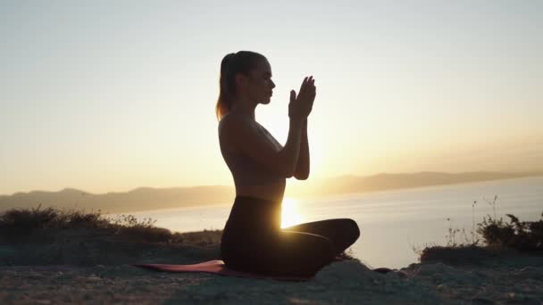 Silueta de mujer practica yoga sobre estera y medita al amanecer, cámara lenta — Vídeo de stock