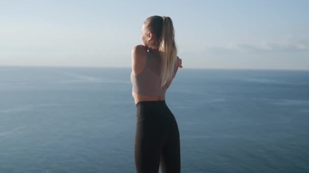 Retrovisore di ragazza che fa esercizi sulla scogliera con vista sull'oceano, rallentatore — Video Stock