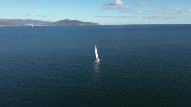 Повітряні кадри білої вітрильної яхти на морській воді в сонячний день, широкий кут зору — стокове відео