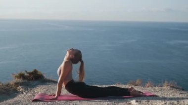 Dağın tepesinde yoga egzersizi yapan kadın, arka planda deniz, yavaş çekim
