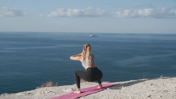 Slim woman makes crouches outdoors, trains her body, with sea view, slow motion — Stock Video