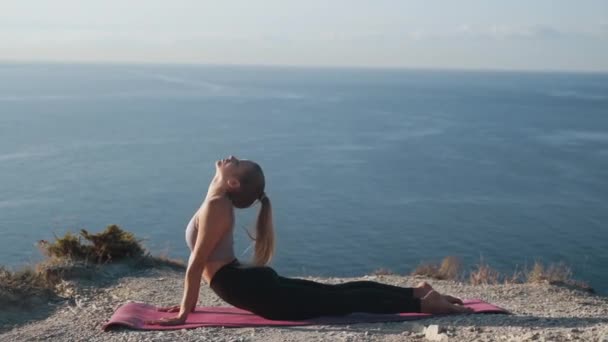 Γυναίκα κάνει γιόγκα άσκηση στην κορυφή του βουνού, θάλασσα στο παρασκήνιο, αργή κίνηση — Αρχείο Βίντεο
