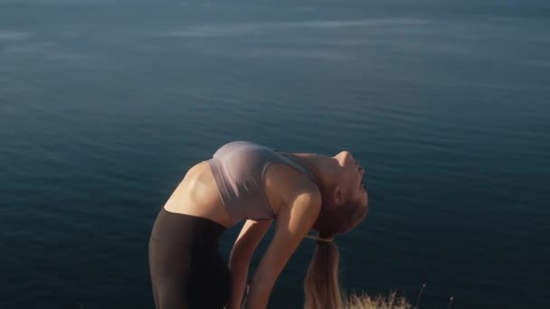 Mulher faz exercícios e se estende ao nascer do sol com vista para o mar, câmera lenta — Vídeo de Stock