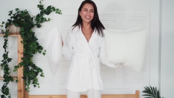 Šťastná žena v županu skáčou na posteli s polštáři, pomalý pohyb. Zábavné video — Stock video