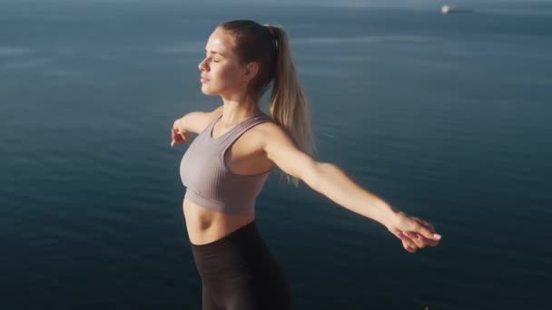 Mujer hace ejercicios y se extiende al amanecer con vista al mar, cámara lenta — Vídeo de stock