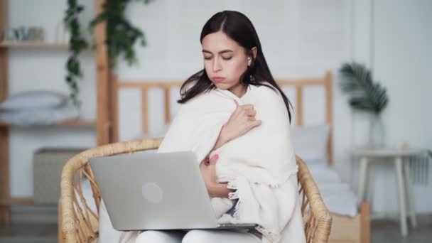 Mulher congelou e envolve-se em xadrez, menina senta-se na cadeira e trabalha no laptop — Vídeo de Stock