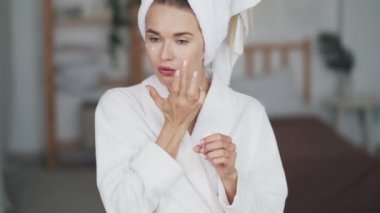  Başında havlu olan kadın yüzüne nemlendirici krem uyguluyor, yakından