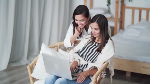 Dvě mladé ženy v ložnici vypadají jako laptopy, usmívají se a diskutují — Stock video