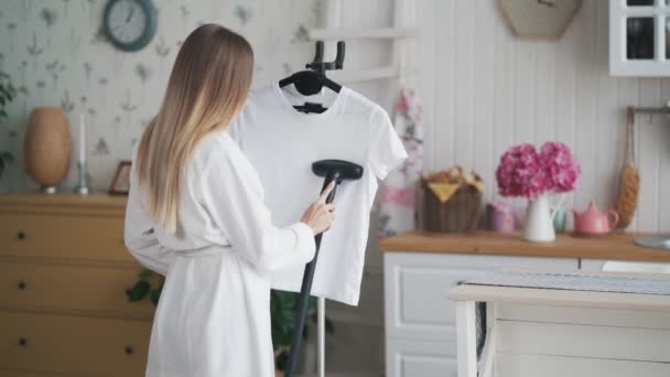 Camiseta de planchar niña en albornoz blanco con vapor en casa — Vídeos de Stock
