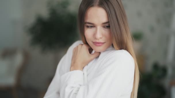 Porträt einer jungen schönen Frau im weißen Bademantel blickt in die Kamera, lächelt — Stockvideo