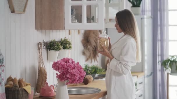 Jeune femme ouvre placard dans la cuisine et sort une boîte de nourriture — Video