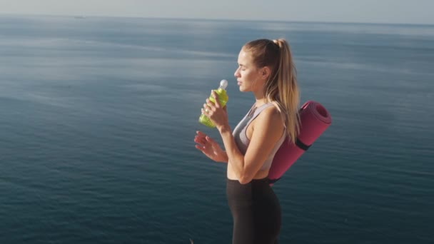 Mujer en ropa deportiva bebe agua de la botella después del entrenamiento cerca del mar, cámara lenta — Vídeo de stock