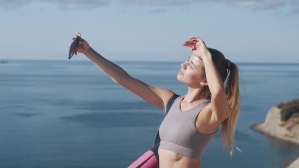 Девушка в спортивной одежде делает селфи по телефону после тренировки, показывает жест мира — стоковое видео