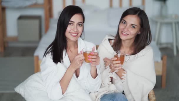 Deux belles filles tiennent des tasses de thé dans leurs mains, regarder la caméra et sourire — Video