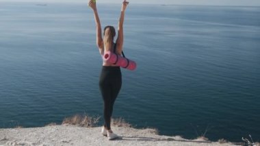 Arka manzara, spor giyimli kadın uçurumun kenarında duruyor, kollarını ardına kadar açıyor.