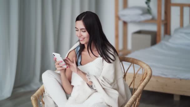 Belle femme brune est assise dans une chaise à carreaux et utilise le téléphone — Video