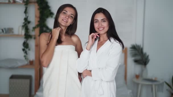 Портрет двух красивых девушек в халатах смотреть в камеру, улыбаться, в спальню — стоковое видео