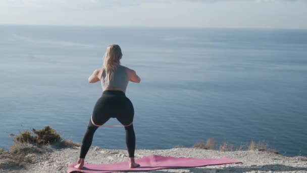 Achteraanzicht vrouw maakt stappen, hurken met rubberen band buiten, slow motion — Stockvideo
