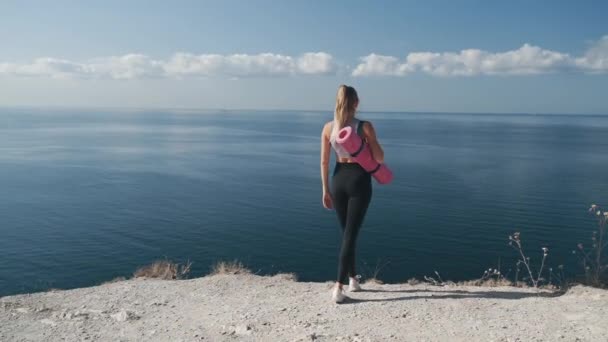 Achteraanzicht, vrouw in sportkleding gaat naar de rand van de klif, opent haar armen wijd — Stockvideo