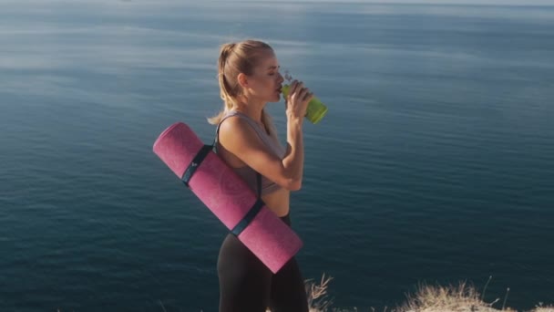 Donna in abbigliamento sportivo beve acqua dalla bottiglia dopo l'allenamento vicino al mare, rallentatore — Video Stock