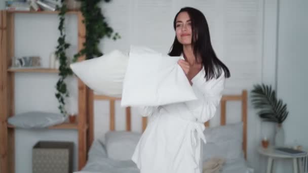 Mujer joven saltando en el dormitorio y bailando con almohadas en casa, video divertido — Vídeos de Stock