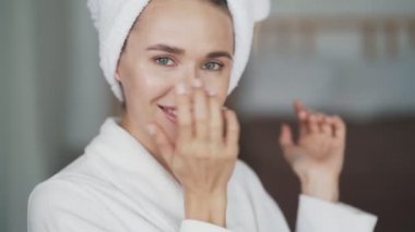 Kafasında havlu olan bornozlu kadın portresi yüzüne krem sürmüş.