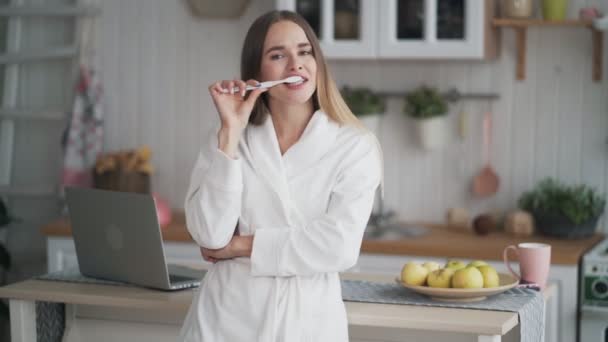 Vacker ung kvinna i badrock borstar tänderna med tandborste på morgonen — Stockvideo