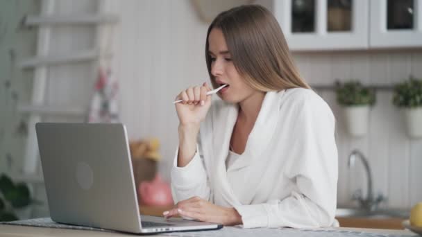 女の子は歯ブラシで彼女の歯を磨き、午前中に電子メールをチェックするためにラップトップを使用 — ストック動画