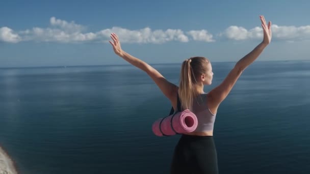 Rückansicht, Frau in Sportbekleidung steht am Rande der Klippe, breitet die Arme weit aus — Stockvideo