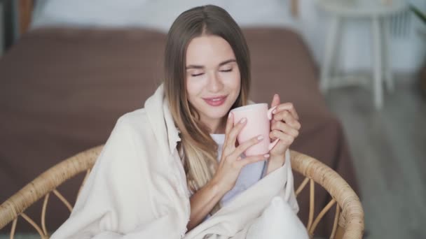 Retrato de mujer sonriente envuelta en cuadros bebe té caliente, mira a la cámara — Vídeo de stock