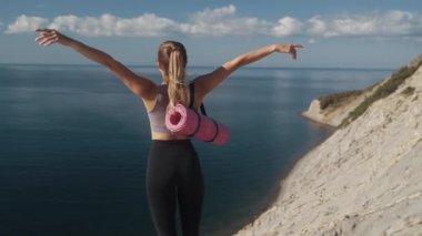 Arka manzara, spor giyimli kadın uçurumun kenarında duruyor, kollarını ardına kadar açıyor.