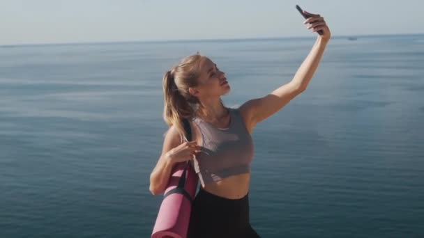 Дівчина в спортивному одязі бере селфі по телефону після тренування, показує жест миру — стокове відео