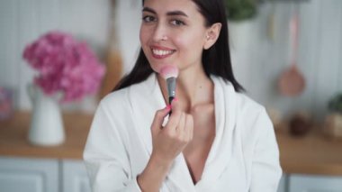 Güzel bir kadının portresi makyaj yapar ve yüzüne pudra sürmek için fırça kullanır.