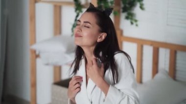 Sabahları beyaz bornozlu genç bir kadın yatakta dans ediyor, müzik dinliyor.
