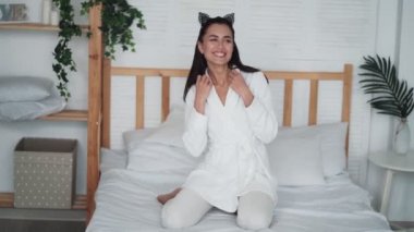 Sabahları beyaz bornozlu genç bir kadın yatakta dans ediyor, müzik dinliyor.