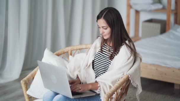 Vacker ung kvinna sitter i fåtölj och använder laptop. Frilansare arbetar hemma — Stockvideo