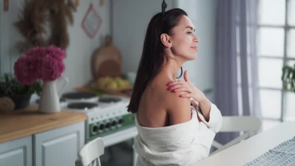 Jonge vrouw in badjas brengt crème aan op lichaam, schouder, huid hydraterende — Stockvideo