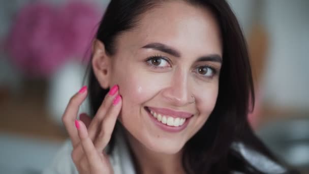 Retrato de mujer en albornoz aplica crema en su cara y hace masaje facial — Vídeo de stock