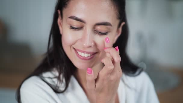 Retrato de mujer en albornoz aplica crema en su cara y hace masaje facial — Vídeo de stock