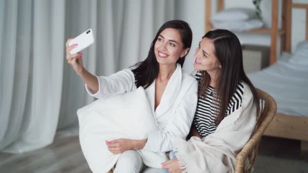 Dos chicas toman selfie en el teléfono, posando, muestran gesto de paz, sonriendo en casa — Vídeos de Stock