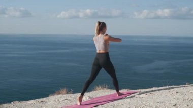 Kadın dışarıda çömeliyor, vücudunu eğitiyor, deniz manzaralı, arka manzaralı.