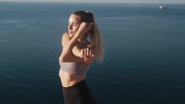 Frau macht Übungen und dehnt sich bei Sonnenaufgang mit Blick auf das Meer, Zeitlupe — Stockvideo