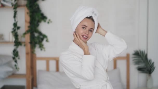 Wanita muda yang cantik dengan jubah mandi dan dengan handuk di kepalanya menari di kamar tidur — Stok Video